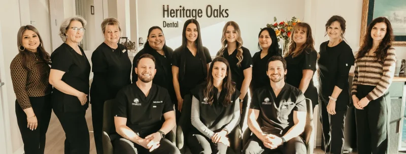 Group portrait of the Heritage Oaks Dental team, featuring doctors seated in front and staff members standing in a modern clinic lobby under pendant lighting